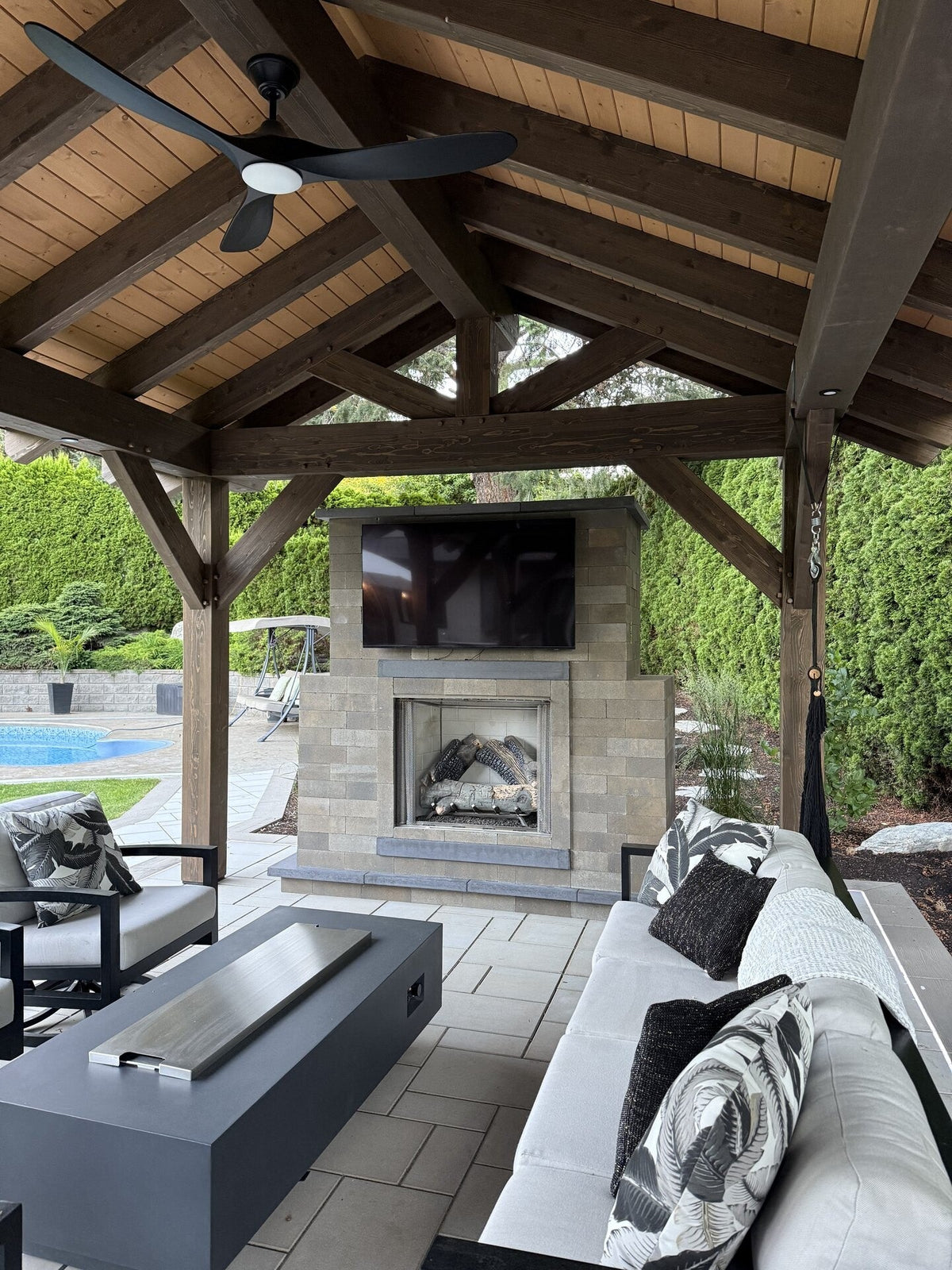 Covered outdoor living area from DAB-T Contracting’s showcase, with timber pavilion, masonry fireplace, seating and paver patio